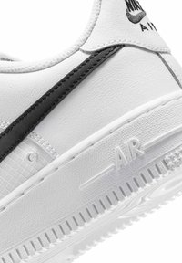 Close-up of white sneaker with black Nike swoosh, textured sole embossed with "AIR," and padded ankle collar.