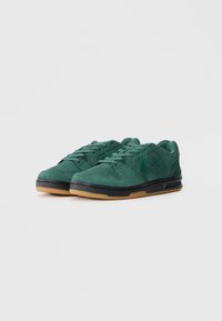 Adidași din suede verde, cu talpă din cauciuc, având un logo în formă de stea, sistem de încheiere cu șireturi și detalii texturate pe partea superioară.