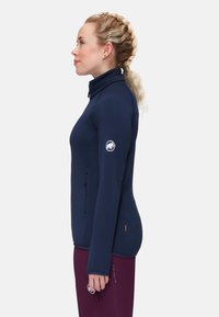 Giacca a maniche lunghe blu navy con collo alto, tasca laterale con zip e logo sulla spalla. Tessuto liscio e design aderente.