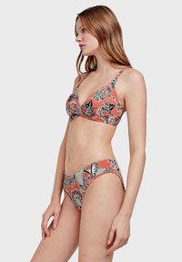 Ensemble de maillot de bain avec un fond corail et des motifs floraux et paisley noirs. Le soutien-gorge a une forme triangulaire ; le bas de bikini est taille basse.