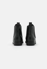 Bottes cheville en cuir noir avec panneaux latéraux élastiques, languettes de tirage et semelles plates. Le design est épuré avec des coutures visibles minimales.