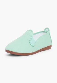 Chaussure slip-on vert clair à bout arrondi, dessus en tissu, côtés élastiques, boucle au talon et semelle plate marron.