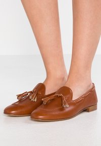 Bruine leren instappers met franjes, ronde neus en minimale stiksels. Lage houten hak en een gladde textuur.