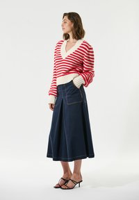 Maglione a righe rosse e bianche con scollo a V e orlo a coste, abbinato a una gonna di jeans blu con tasche laterali e forma svasata.