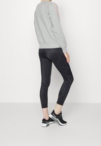 Felpa grigia con maniche lunghe abbinata a leggings neri con un motivo geometrico di piccoli pois. Indossate scarpe da ginnastica nere.
