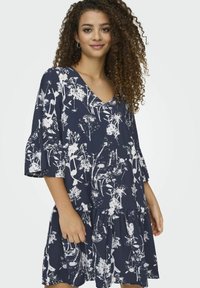 Robe marine avec motif floral blanc, décolleté en V, manches évasées et ourlet en cascades. Fabriquée en tissu doux et léger.