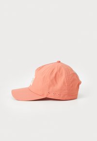 Korallfarget baseballcaps laget av lett stoff, med buet skjerm, brodert lapp foran og ventilasjonsluftehull på sidene.