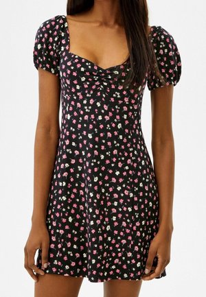 Robe noire à fleurs avec de courtes manches bouffantes, présentant un corsage ajusté et une jupe fluide. De petites fleurs roses et blanches créent un motif répétitif.