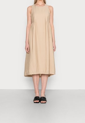 Beige mouwloos jurk met een ronde halslijn en een geplooide taille, met een middellange zoom. Gecombineerd met zwarte geweven slip-on sandalen.