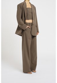 Veste marron sur mesure avec des accents cloutés, associée à un top court assorti et un pantalon à jambes larges, avec des détails cloutés sur les côtés.