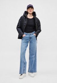 Prešívaná čierna bunda s kapucňou, čierne tričko s dlhým rukávom, svetlomodré široké rifle a biele tenisky. Model má na hlave tmavú šiltovku. Jednoduché pozadie.