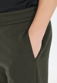 Groene katoenen joggingbroeken zijn voorzien van een elastische tailleband en zijzakken. De stof heeft een gladde textuur met zichtbare stikdetails.