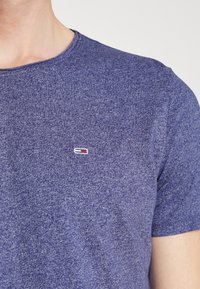 Kurzärmliges T-Shirt mit Rundhalsausschnitt aus meliertem Dunkelblau mit einem kleinen gestickten Logo in Rot und Weiß auf der Brust.
