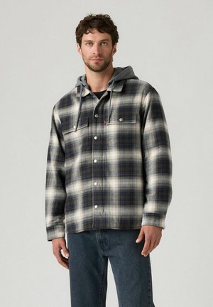 Flannel jacket in black, white, and blue plaid. Features a gray hood, front buttons, and two chest pockets. Stylish, relaxed fit.
