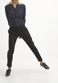 Pantaloni neri su misura con orli risvoltati, abbinati a una camicia blu con pois e scarpe da ginnastica nere, caratterizzati da una vestibilità rilassata e una texture sottile.