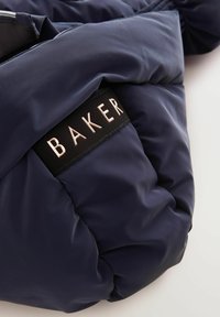 Námornícky prešívaný puff puffer kabát s čiernou textilnou nášivkou s nápisom "BAKER" v metalickej zlatej farbe, textúrovaný povrch a hladké zipsy.