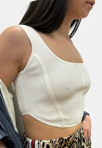 Top corto bianco a coste con scollatura quadrata, dotato di cuciture laterali e un design aderente. Indossato con pantaloni a fantasia, che mostrano un tessuto testurizzato.