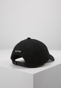 Fekete pamut baseball sapka ívelt karimával, a hátsó részen fehér hímzéssel "EST.1922" felirattal, állítható műanyag pántos záródással.