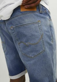Shorts de mezclilla en azul claro, con dobladillo enrollado, costura amarilla contrastante y dos bolsillos traseros con costuras curvas. Etiqueta de piel en la cinturilla.