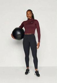 Urheilullinen asu, joka koostuu tiukasta burgundinpunaisesta pitkähihaisesta paidasta ja mustista leggins-housuista, yhdistettynä mustiin urheilukenkiin ja mustaan lääkepalloon.