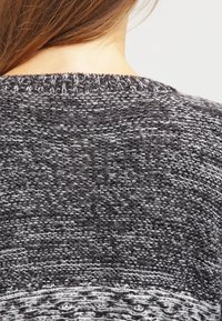 Stickad tröja i nyanser av grått med en texturerad mönstring. Har en löst sittande design och ribbad halsringning. Mjuk, avslappnad tyg.