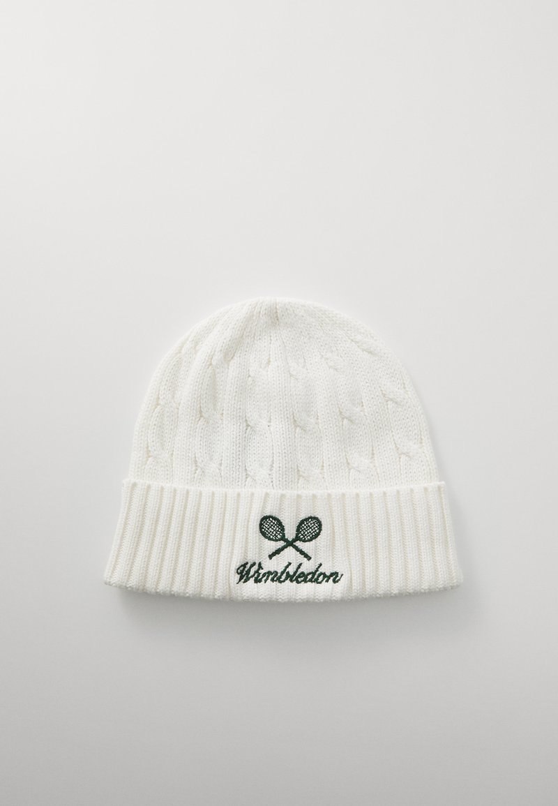 Valge kootud beanie, millel on nöörmustrit, soonikserv ja roheline broderi "Wimbledon" logo, kus on ristatud tennise reketid.