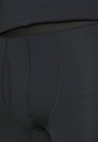 Czarne sportowe legginsy z gładką fakturą, elastycznym pasem i widocznymi szwami, zaprojektowane z myślą o komforcie i swobodzie ruchów.