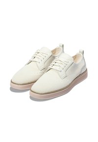 Scarpe bianche in rete con lacci, dalla superficie testurizzata, punta rotonda e cuciture sottili. Presentano una suola in gomma beige e una linguetta sul retro.
