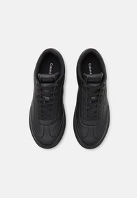 Sorte sneakers med en glatt skinnoverdel, rund tupp, teksturerte detaljer og flate lisser. Har en logo på tungen og teksturert såle.