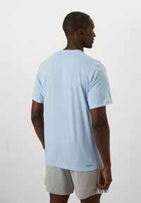 Lichtblauw T-shirt met korte mouwen, gemaakt van zachte stof, met een ronde halslijn en een subtiele logo nabij de zoom. Eenvoudig en casual ontwerp.
