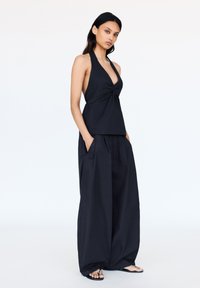 Černý halter top s detailním zkroucením vpředu, spojený s volnými širokými černými kalhotami. Model má na sobě ploché černé sandály.