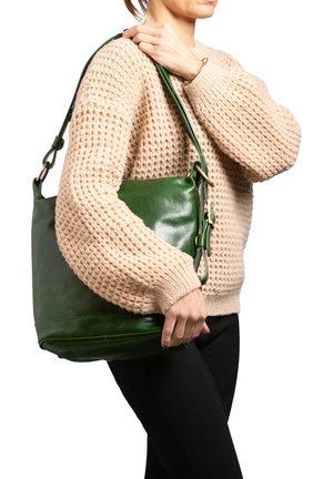 Borsa a tracolla in pelle verde con una texture liscia, arricchita da dettagli in oro. Indossata sopra un maglione beige.