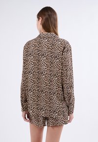 Setti loungewear kanssa leopardi-kuosiset, jossa on pitkähiardinen paita ja lyhyet housut vaaleanruskeissa ja tummaruskeissa sävyissä, pehmeällä pinnalla ja rentolla istuvuudella.