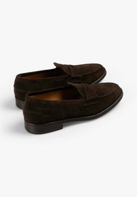 Mocasines de ante marrón oscuro con punta redondeada, costuras decorativas y un tacón bajo. Textura suave y diseño sin cordones.