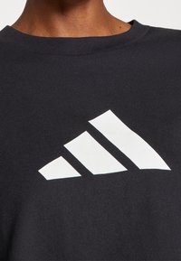 Černé bavlněné tričko s výrazným bílým logem se třemi pruhy na hrudi. Klasický kulatý výstřih a hladká textura.