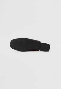 Brown textured shoe with a matte black rubber sole and a square heel. Features a patterned upper for grip and durability.