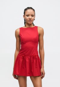 Červené šaty bez rukávů s přiléhavým živůtkem a nařasenou sukní. Má stahovací šňůrky v pase. Hladká látka, minimalistický design.