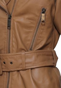 Braune Lederjacke mit einer sichtbaren Reißverschlusstasche, einem breiten Gürtel und einer glatten Textur. Das Design umfasst eine elegante Silhouette.