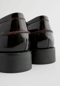 Chaussures en cuir verni noir avec un bout rond, des détails de couture subtils et un talon noir solide et texturé. Fini lisse et brillant.