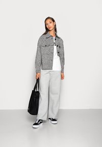 Chaqueta gris texturizada con bolsillos frontales, camiseta blanca, pantalones anchos grises, bolso negro y zapatillas negras con suelas blancas.