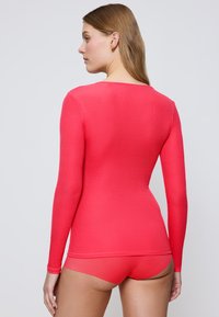 Langarmoberteil und passende Unterwäsche in Korallenpink. Das Oberteil hat eine gerippte Textur und einen runden Ausschnitt, der den Körper eng umschließt.