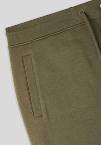 Oliwkowe spodnie dresowe z ribbowanym paskiem w talii, sznurkiem do ściągania i kieszenią boczną. Gładka tekstura i luźny krój.