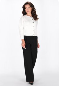 Cardigan alb, cu nasturi, cu un model texturat și mâneci lungi, asortat cu pantaloni negri, largi, și pantofi negri cu vârf ascuțit.