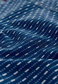 Tissu bleu marine avec une surface texturée, présentant des rayures blanches verticales et des motifs en zigzag. Texture douce et tissée avec un éclat subtil.