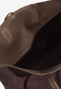 Bruine suède draagtas met een gladleren interieur. Voorzien van gestikte accenten en een open bovenkant voor gemakkelijke toegang tot de inhoud.