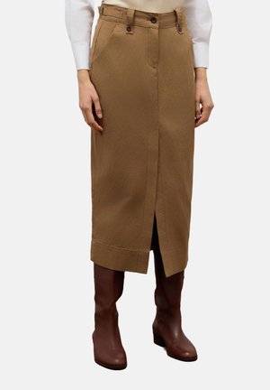 Knie-lange, brown cotton rok met een voorknof, twee zijzakken en een knoopsluiting op de tailleband. G gedragen met bruin kniehoge laarzen.