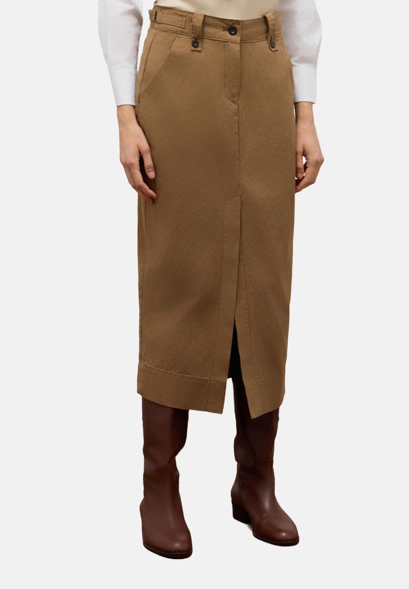 Knie-lange, brown cotton rok met een voorknof, twee zijzakken en een knoopsluiting op de tailleband. G gedragen met bruin kniehoge laarzen.