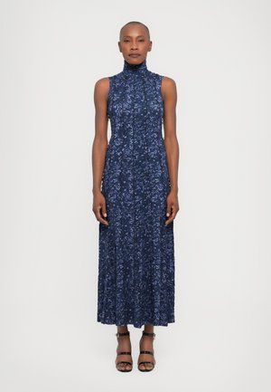 Rochie fără mâneci, cu imprimeu floral într-o nuanță de albastru marin, gât înalt, design pliat și fustă până la gleznă. Asortată cu sandale negre cu bretele.
