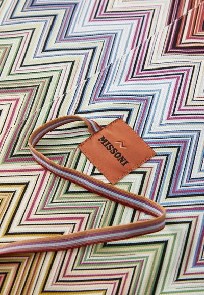Missoni tkanina s uzorkom u obliku zig-zag u živopisnim bojama poput ružičaste, zelene i plave, s bež oznakom koja prikazuje naziv brenda.