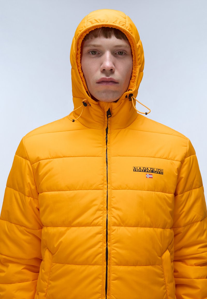 Giacca puffer gialla con cappuccio, texture trapuntata, zip frontale e logo sul petto. Presenta cordini sul cappuccio per la regolazione.